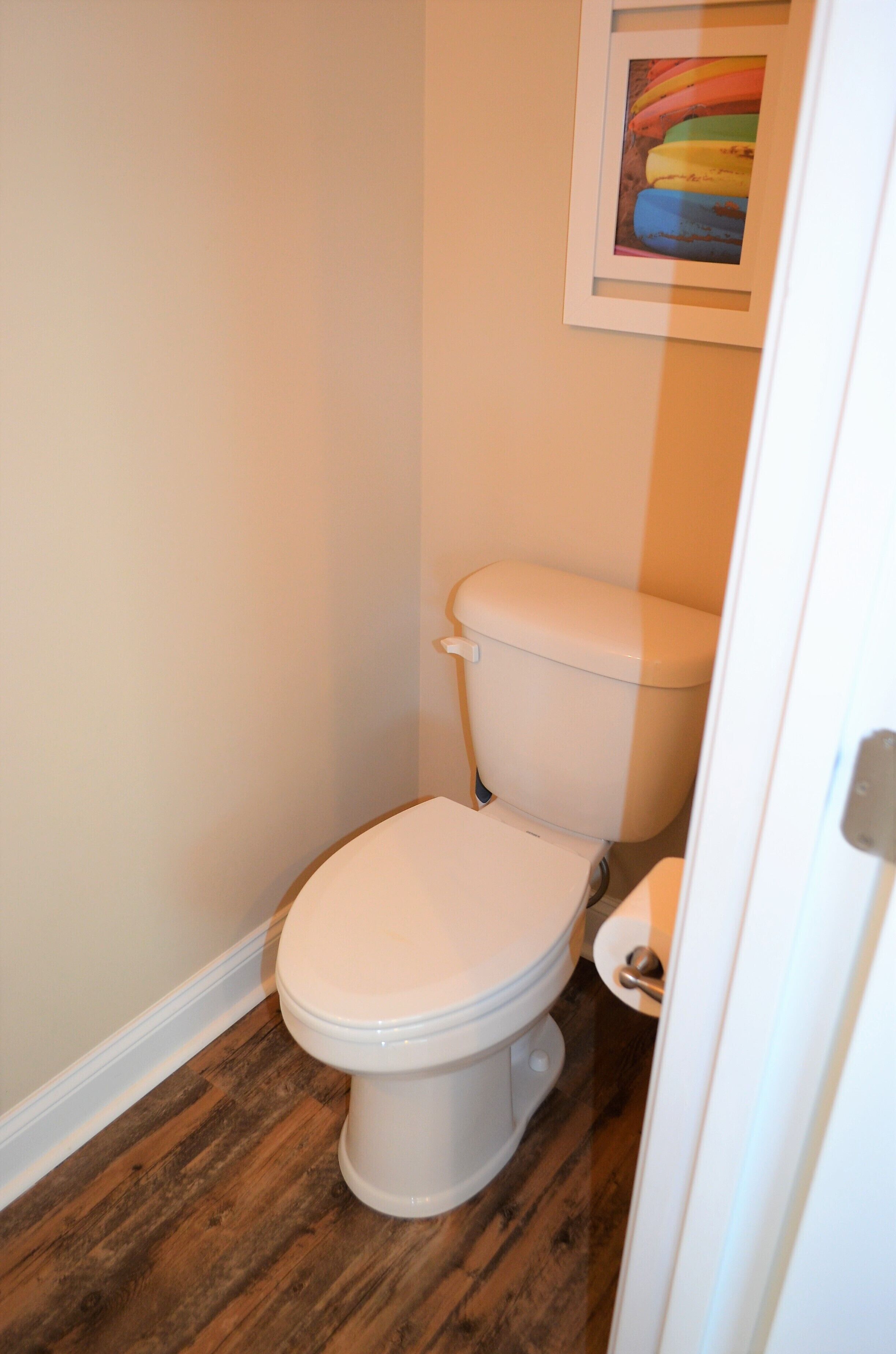 A small, compact bathroom with a white toilet, wooden flooring, and a framed picture on the wall.