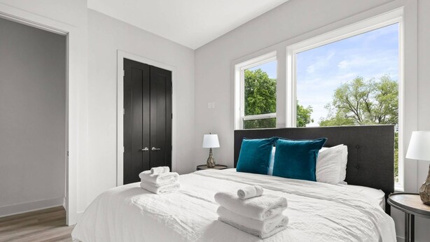 A hotel room with a large bed, two nightstands, a dark door, and a window with a view of trees. - H18 ~ Large Condo w/ Private Rooftop with Downtown Views ~ Garage Parking ~ 9 Minute to Broadway (Nashville)