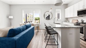 A modern kitchen with white cabinets, a central island with bar stools, and a dining area with a blue sofa. - H18 ~ Large Condo w/ Private Rooftop with Downtown Views ~ Garage Parking ~ 9 Minute to Broadway (Nashville)