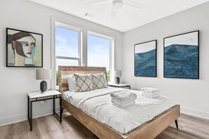 Une chambre à coucher moderne avec un lit en bois, deux tables de chevet, une petite table et des œuvres d’art accrochées aux murs.