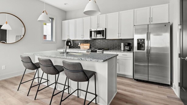 Eine moderne Küche mit weißen Schränken, einem Edelstahl-Kühlschrank, einer Mikrowelle und einer Kücheninsel mit Granitplatte und Barhocker.