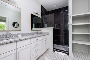 A modern bathroom with a granite countertop, a large mirror, a shower with black tiles, and a white tiled floor. - H16 ~ 4 Private Suites ~ Huge Private Rooftop ~ 6 Beds ~ 8 Minutes to Downtown (Nashville)