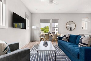 A modern living room with a blue sofa, a coffee table, and a TV mounted on the wall. - H16 ~ 4 Private Suites ~ Huge Private Rooftop ~ 6 Beds ~ 8 Minutes to Downtown (Nashville)