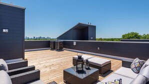 Eine Dachterrasse mit Gartenmöbeln, Blick auf die Stadtlandschaft und einem modernen Gebäudebau.