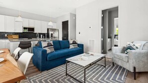 Eine moderne Wohnung mit Küche, einem blauen Sofa, einem grauen Sessel und einem Essbereich.