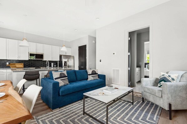 A modern apartment with a kitchen, a blue sofa, a grey armchair, and a dining area. - H16 ~ 4 Private Suites ~ Huge Private Rooftop ~ 6 Beds ~ 8 Minutes to Downtown (Nashville)