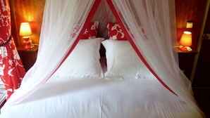 Un lit à baldaquin, deux lampes de chevet et un oreiller à motifs rouges et blancs.