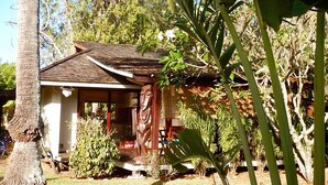 Une petite maison avec un toit en pente, entourée de verdure et d’un palmier.