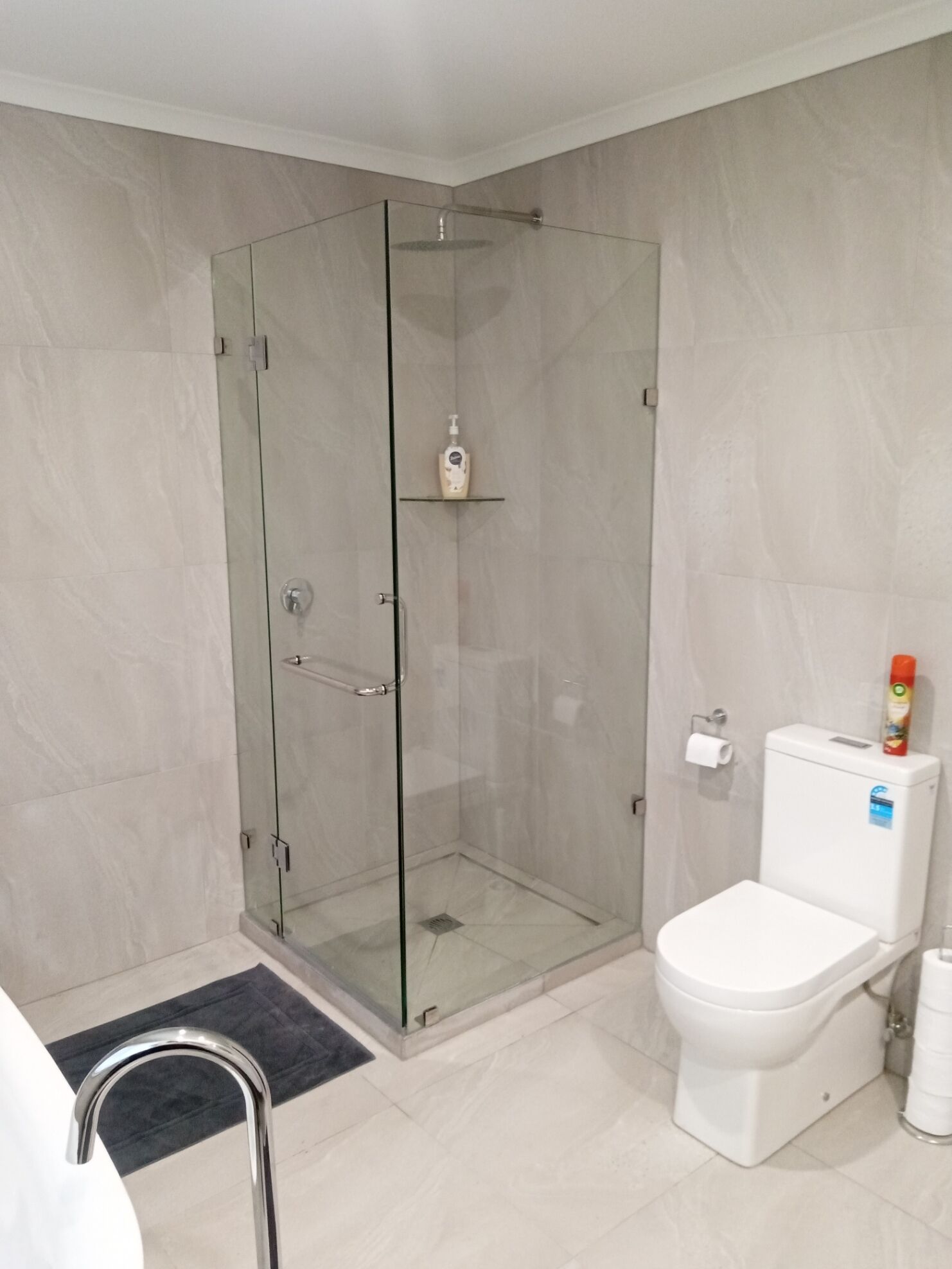 Een moderne badkamer met een glazen douchecabine, een wit toilet en een klein plankje met toiletartikelen.