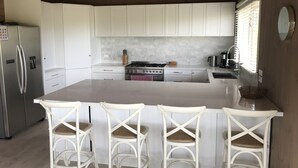 A modern kitchen with white cabinets, a central island with bar stools, a stainless steel refrigerator, and a ceiling fan. - Spacious ocean view beach house - sleeps 12 (Smiths Beach)
