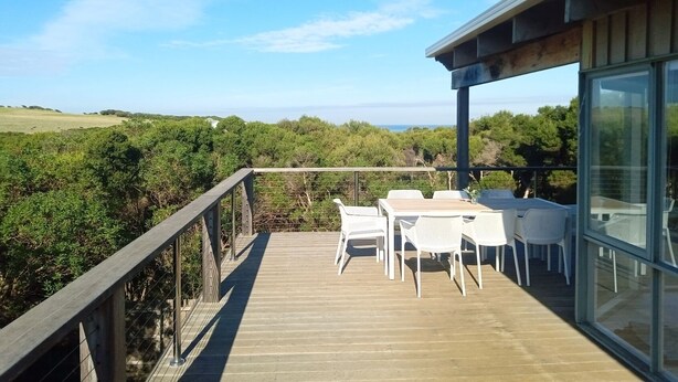 A wooden deck with outdoor furniture, overlooking a natural landscape and a clear sky. - Spacious ocean view beach house - sleeps 12 (Smiths Beach)