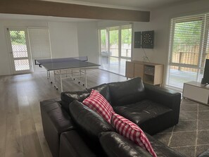 A living room with a ping pong table, a leather sofa with a striped pillow, and a television on a stand. - Spacious ocean view beach house - sleeps 12 (Smiths Beach)