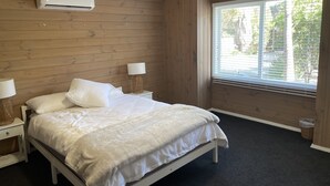 A bedroom with a bed, two bedside tables with lamps, a ceiling fan, an air conditioning unit, and a window with blinds. - Spacious ocean view beach house - sleeps 12 (Smiths Beach)