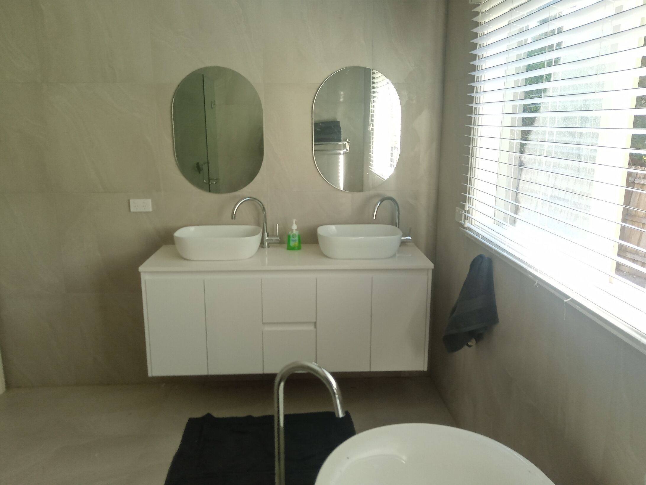 Un baño con dos lavamanos, un espejo y una ventana con persianas.