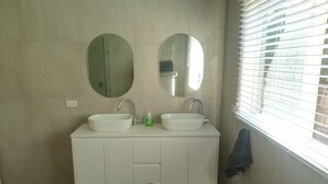 Une salle de bain avec deux lavabos, un miroir et une fenêtre avec des stores.