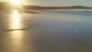 Une plage avec un ciel dégagé et le soleil qui se reflète sur le sable mouillé.