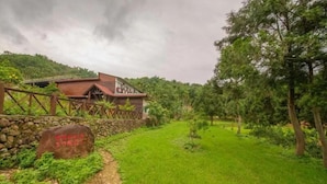 A rustic building with a stone wall and a wooden fence, surrounded by lush greenery and a clear path leading to it. - North Mountain Farm (Puli)