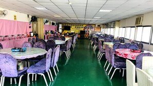 A spacious dining hall with rows of tables and chairs, a green floor, and a banner with text in the background. - North Mountain Farm (Puli)