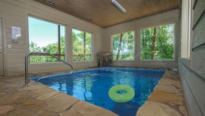 An indoor swimming pool with stone flooring, a metal ladder, and a green inflatable ring. - Hibernation Hideaway - Private indoor pool, theater room, hot tub, games, and more! (Pigeon Forge)