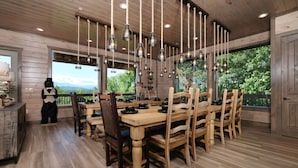 A wooden dining area with a large table and chairs, hanging light fixtures, and a view of greenery outside. - Hibernation Hideaway - Private indoor pool, theater room, hot tub, games, and more! (Pigeon Forge)