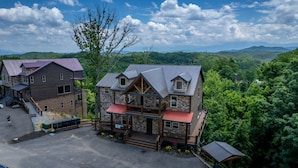 A multi-story lodge with a stone facade, wooden balconies, and a red roof. - Hibernation Hideaway - Private indoor pool, theater room, hot tub, games, and more! (Pigeon Forge)