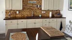 A kitchen with white cabinets, a wooden backsplash, a sink, and a dining table with a placemat. - Agua de copano (Rockport)