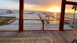A wooden deck with a view of the sunset over the ocean, a pier, and a gazebo. - Agua de copano (Rockport)