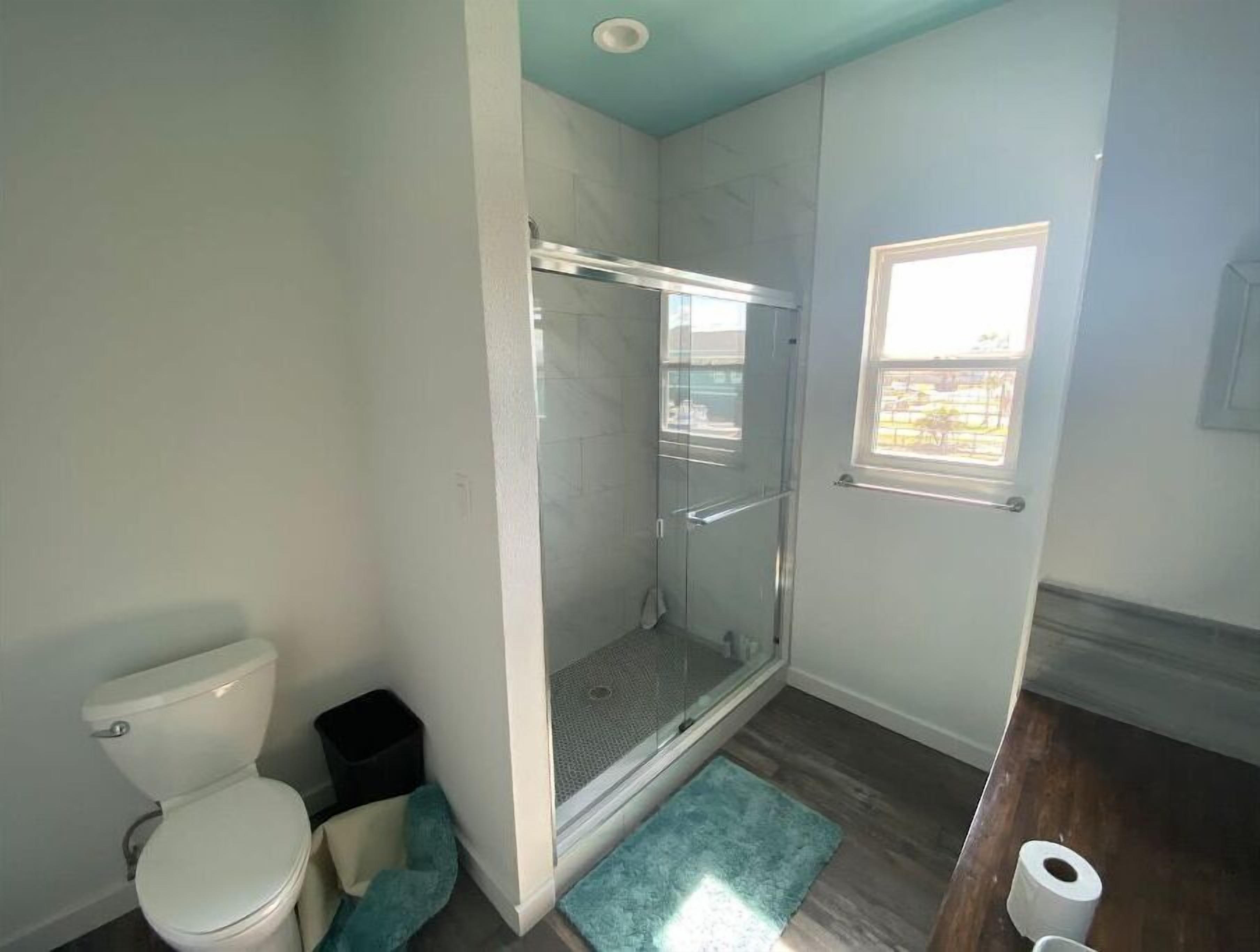 Un bagno con un water, una doccia con porta in vetro, un piccolo finestrino e pavimento in legno.