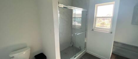 Un bagno con un water, una doccia con porta in vetro, un piccolo finestrino e pavimento in legno.