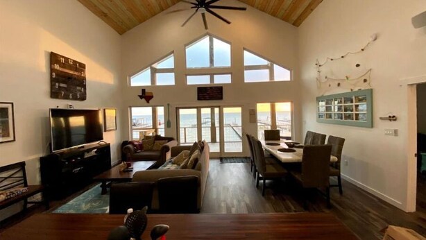 A spacious living room with a high ceiling, large windows, and a dining area. - Agua de copano (Rockport)