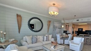 A living room with a sofa, armchairs, a coffee table, and a dining area with a table and chairs. There is a kitchen visible in the background. - Extra Large Balcony Phoenix VII 3/2 Flash Sale (Orange Beach)
