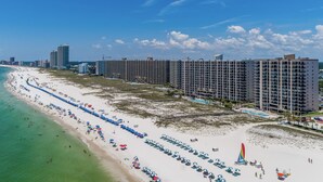 A beachfront hotel with multiple high-rise buildings, a sandy beach with rows of umbrellas, and a clear blue sky. - Extra Large Balcony Phoenix VII 3/2 Flash Sale (Orange Beach)