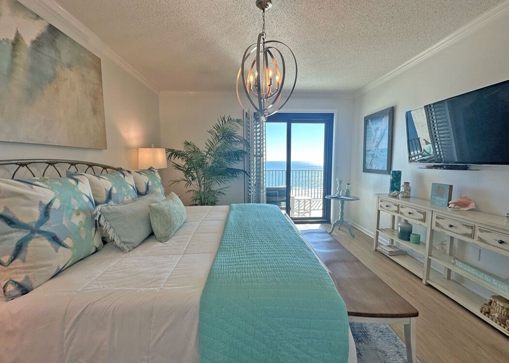 Quarto com uma cama grande, um candelabro, uma TV e uma varanda com vista.
