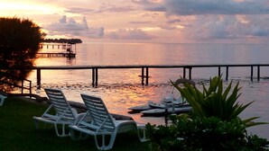 A sunset view over a calm body of water with a pier extending into the water. There are lounge chairs and a small boat docked near the shore. - Premium Suite, lagoon view, 2 bedrooms, kitchen, bathroom (Moorea)