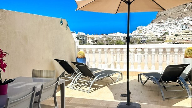 An outdoor patio with a table, chairs, and a large umbrella. - Beautiful three bedroom apartment with shared swimming pool and WIFI (Puerto de Mogan)