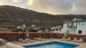 A rooftop pool with lounge chairs, a poolside umbrella, and a view of a mountainous landscape. -  Beautiful Two bedroom apartment with spacious terrace, swimming pool and WIFI (Puerto de Mogan)