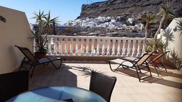 A terrace with a table and chairs, overlooking a white-washed town and a mountain. -  Beautiful Two bedroom apartment with spacious terrace, swimming pool and WIFI (Puerto de Mogan)