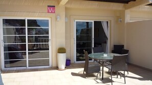 Un espace patio doté d’une porte vitrée, de meubles en osier et d’une plante en pot.