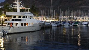 A marina with multiple boats docked, a large yacht in the foreground, and a mountainous backdrop. -  Beautiful Two bedroom apartment with spacious terrace, swimming pool and WIFI (Puerto de Mogan)