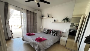 A neatly arranged bedroom with a bed, bedside tables, a ceiling fan, and a view of the outside. -  Beautiful Two bedroom apartment with spacious terrace, swimming pool and WIFI (Puerto de Mogan)
