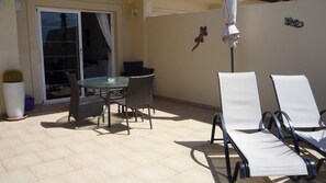 An outdoor patio with a glass table and wicker chairs, a white umbrella, and a cactus plant. - Beautiful Two bedroom apartment with spacious terrace, swimming pool and WIFI (Puerto de Mogan)