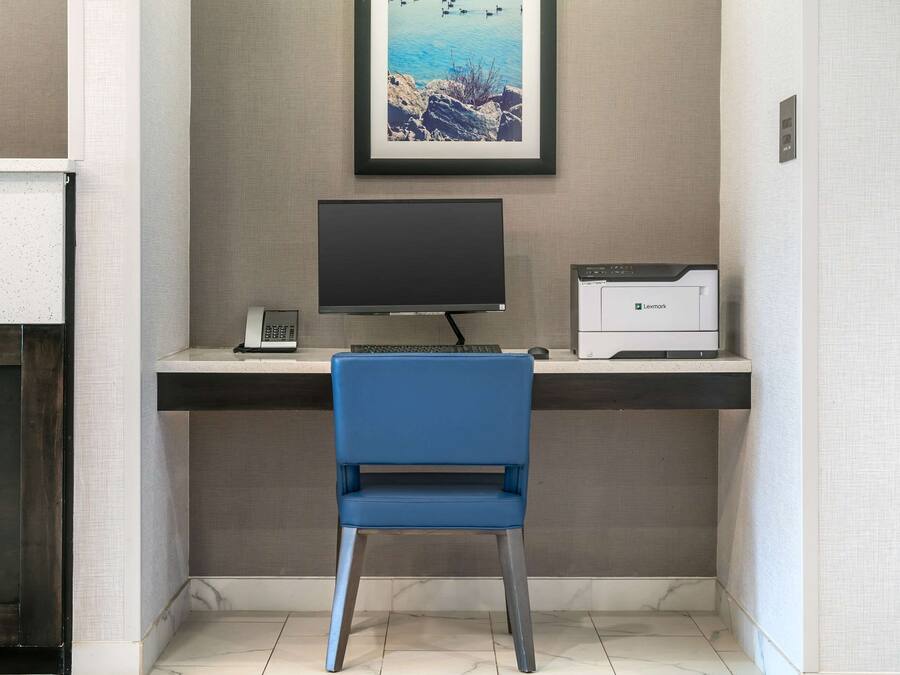 Un escritorio con una computadora, una impresora y un cuadro en la pared.