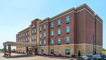 Hotel features a brick facade, flat roof, and rows of windows, with a covered entrance and ample parking.