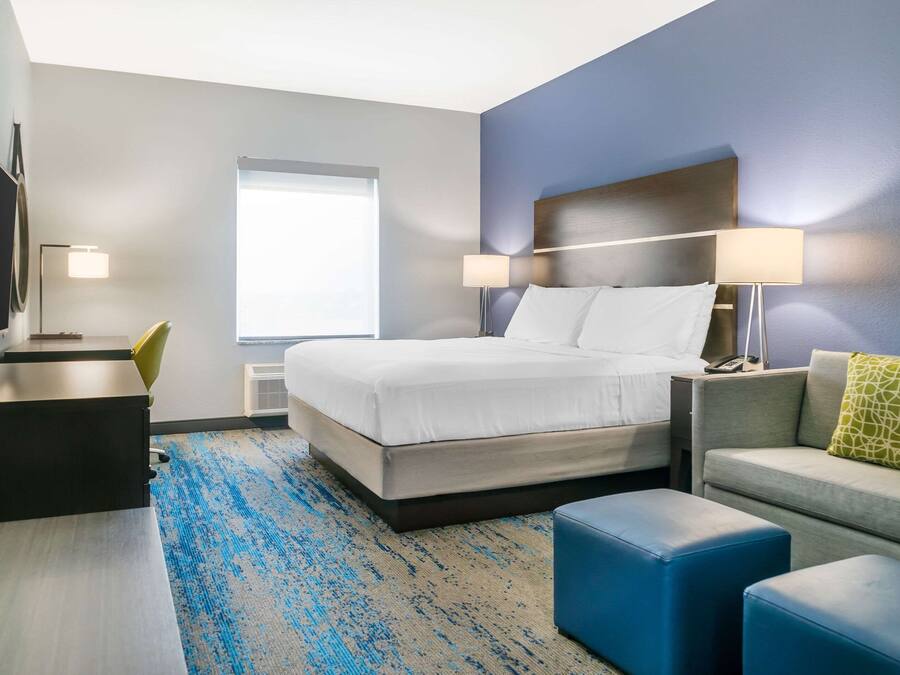 Quarto de hotel com cama, mesas de cabeceira, escrivaninha, poltrona, sofá e televisão.