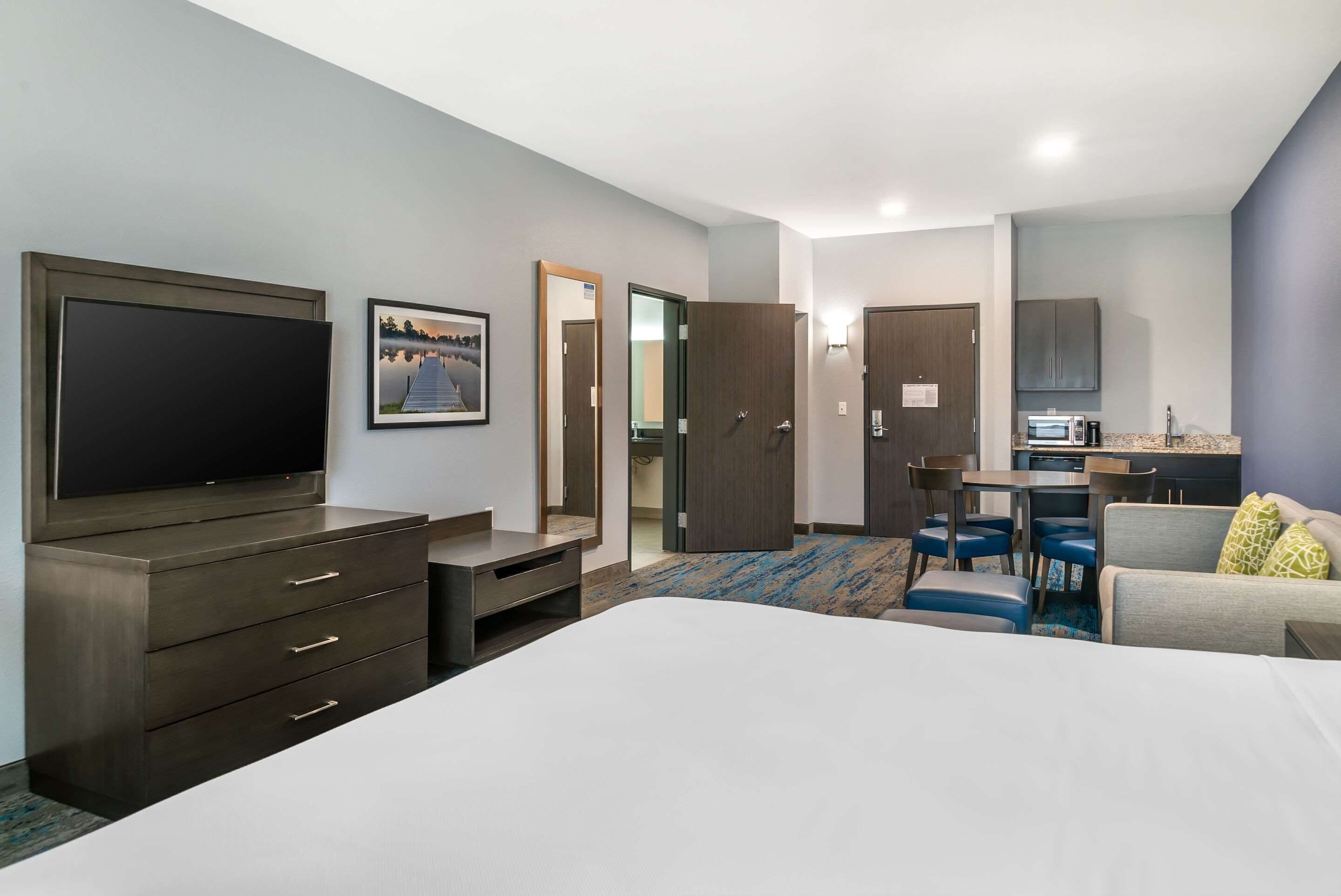A hotel room with a large bed, a TV, a desk with a chair, a microwave, and a small kitchenette.