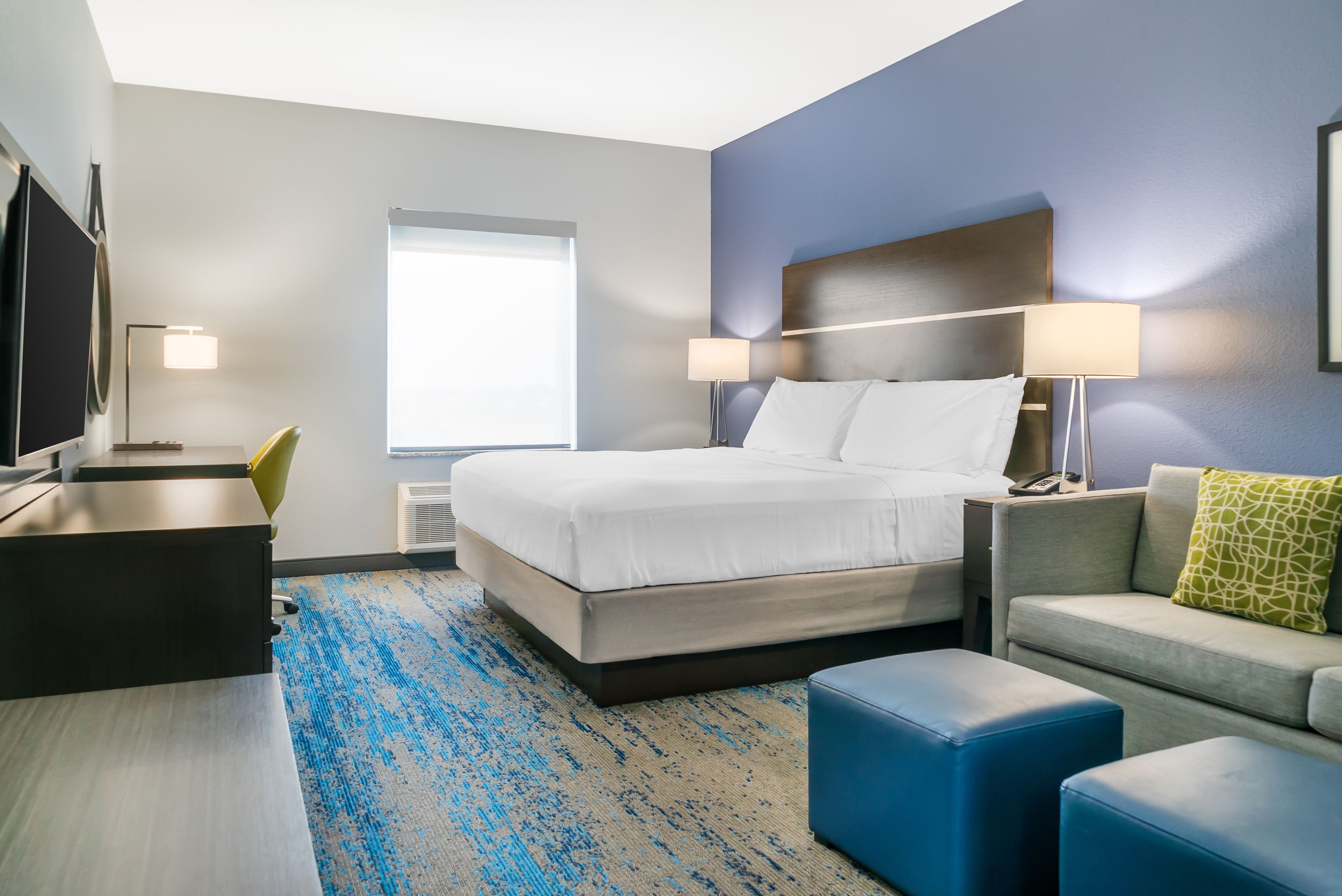 Ein Hotelzimmer mit Bett, Schreibtisch, Stuhl, Sofa und Fernseher.