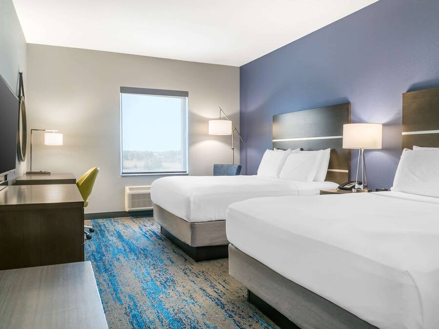 A hotel room with two beds, a desk, a chair, a TV, and a large window.
