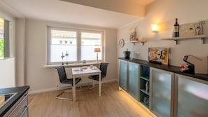 Une cuisine moderne avec une table à manger, des chaises, une machine à café et des verres à vin rangés sur des étagères.