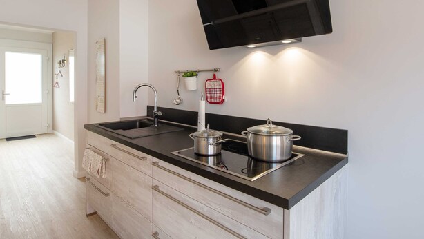 Una cocina moderna con encimera negra, electrodomésticos de acero inoxidable y un televisor de pantalla plana sobre el fregadero.