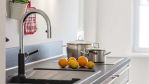 Una cocina con un lavamanos de acero inoxidable, una olla y un paño rojo y blanco a cuadros colgado en la pared.